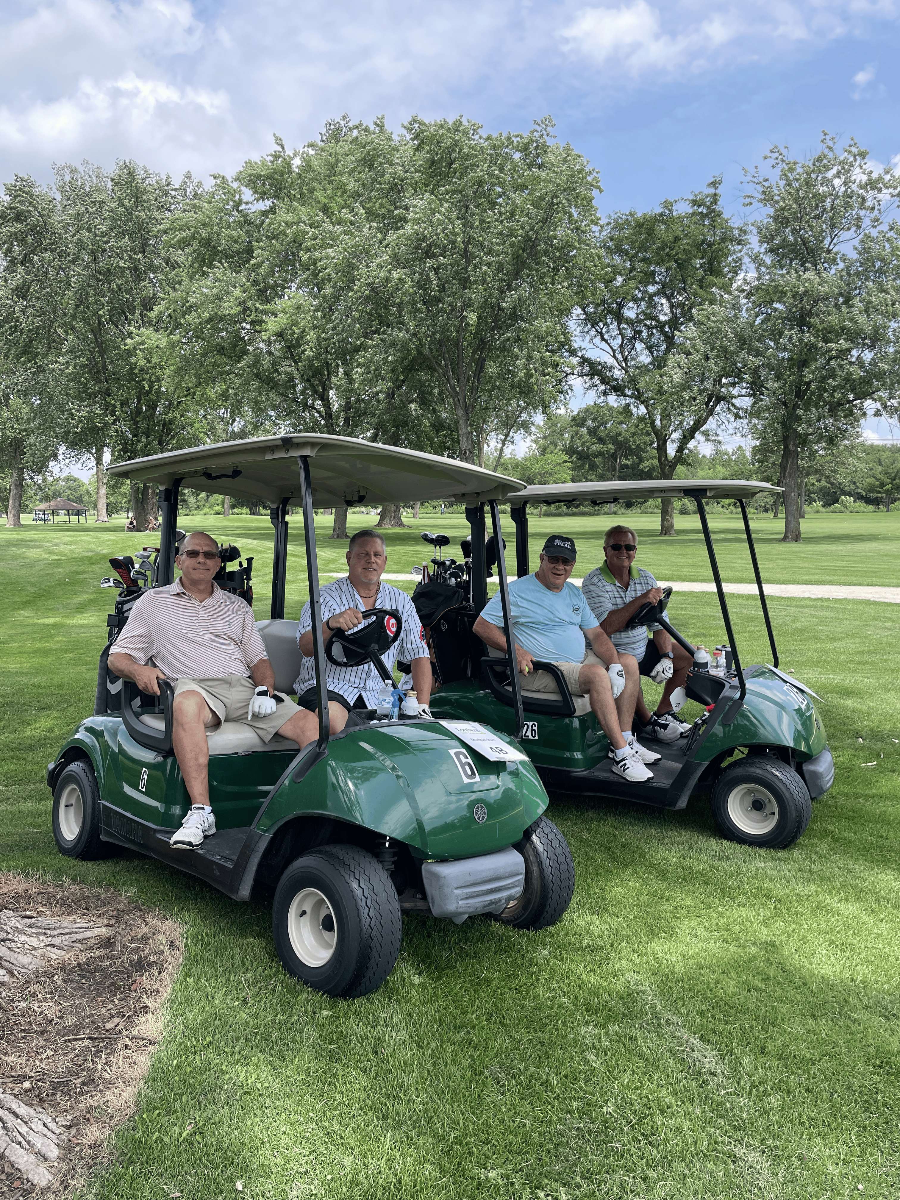 Four golfers in matching outing shirts pose in their golf carts at the inaugural outing